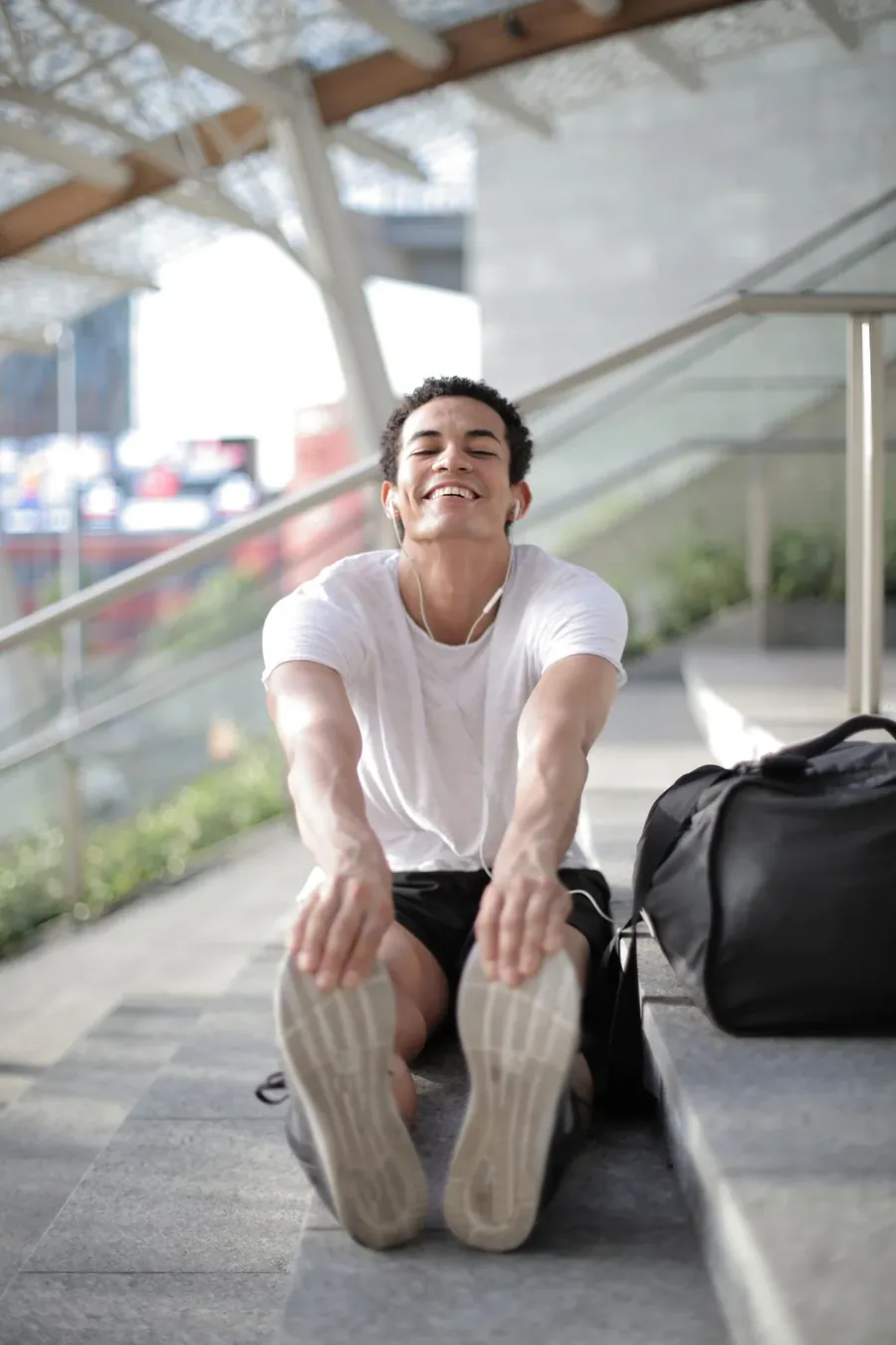 A young man laughs as he stretches his legs on outdoor steps after a workout.