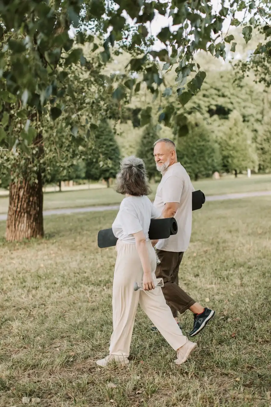 An older couple walking across a park with yoga mats, smiling at each other