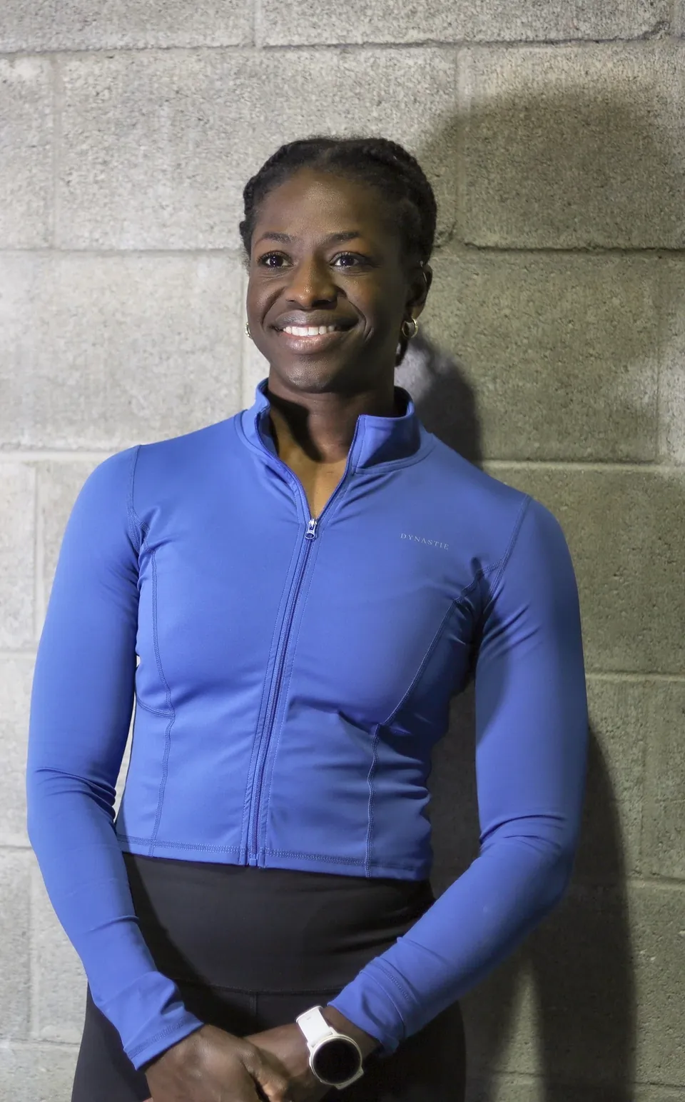 Mivania Henry, ISSA-certified personal trainer, smiling against the block wall at the gym